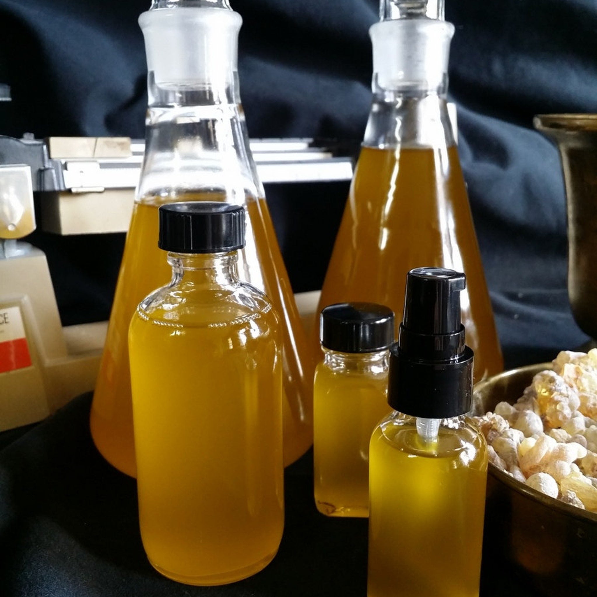 Yellow liquid in glass bottles with black caps and a spray top, next to bowl of resin