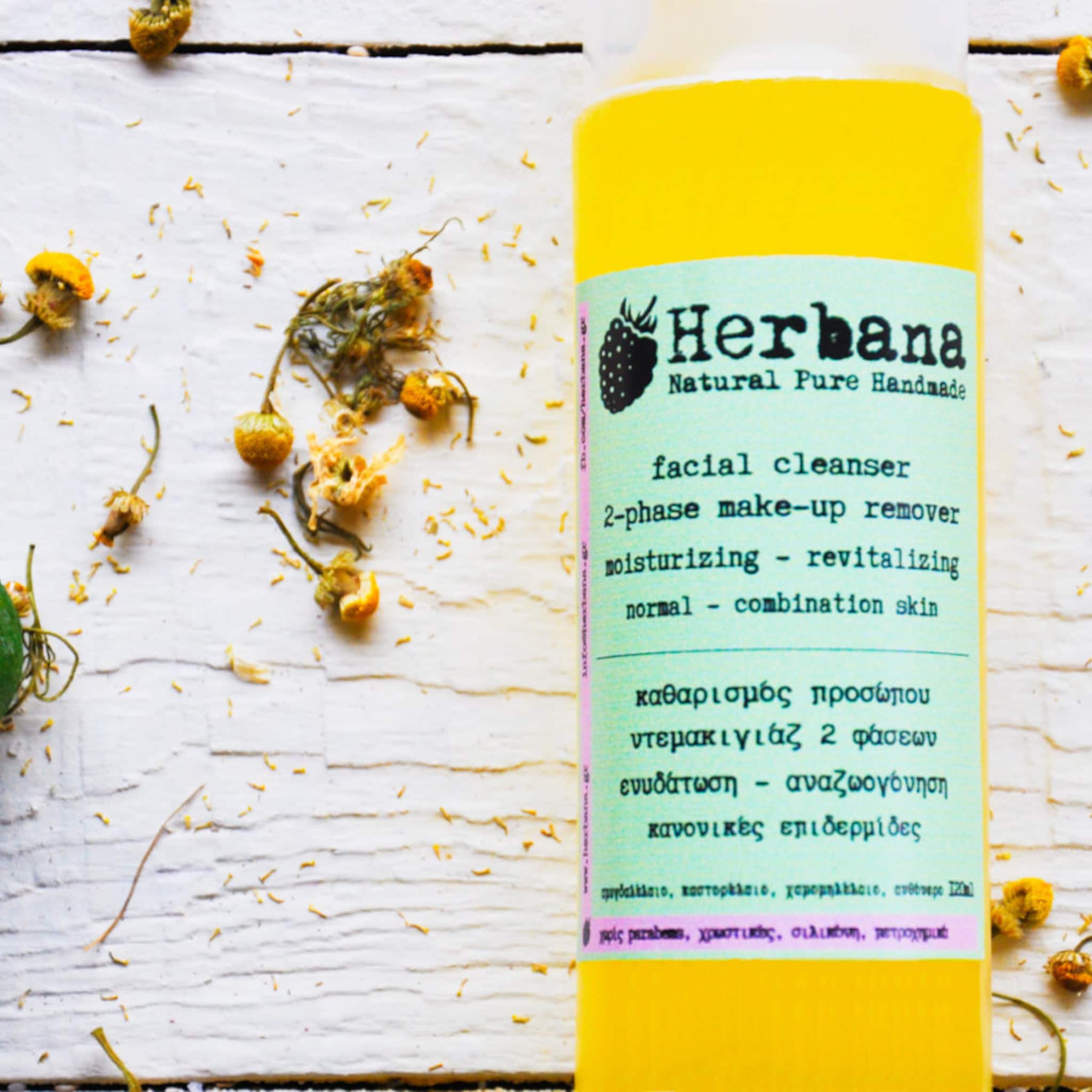 Facial cleanser bottle, yellow liquid, "Herbana" label, white wooden background with dried flowers