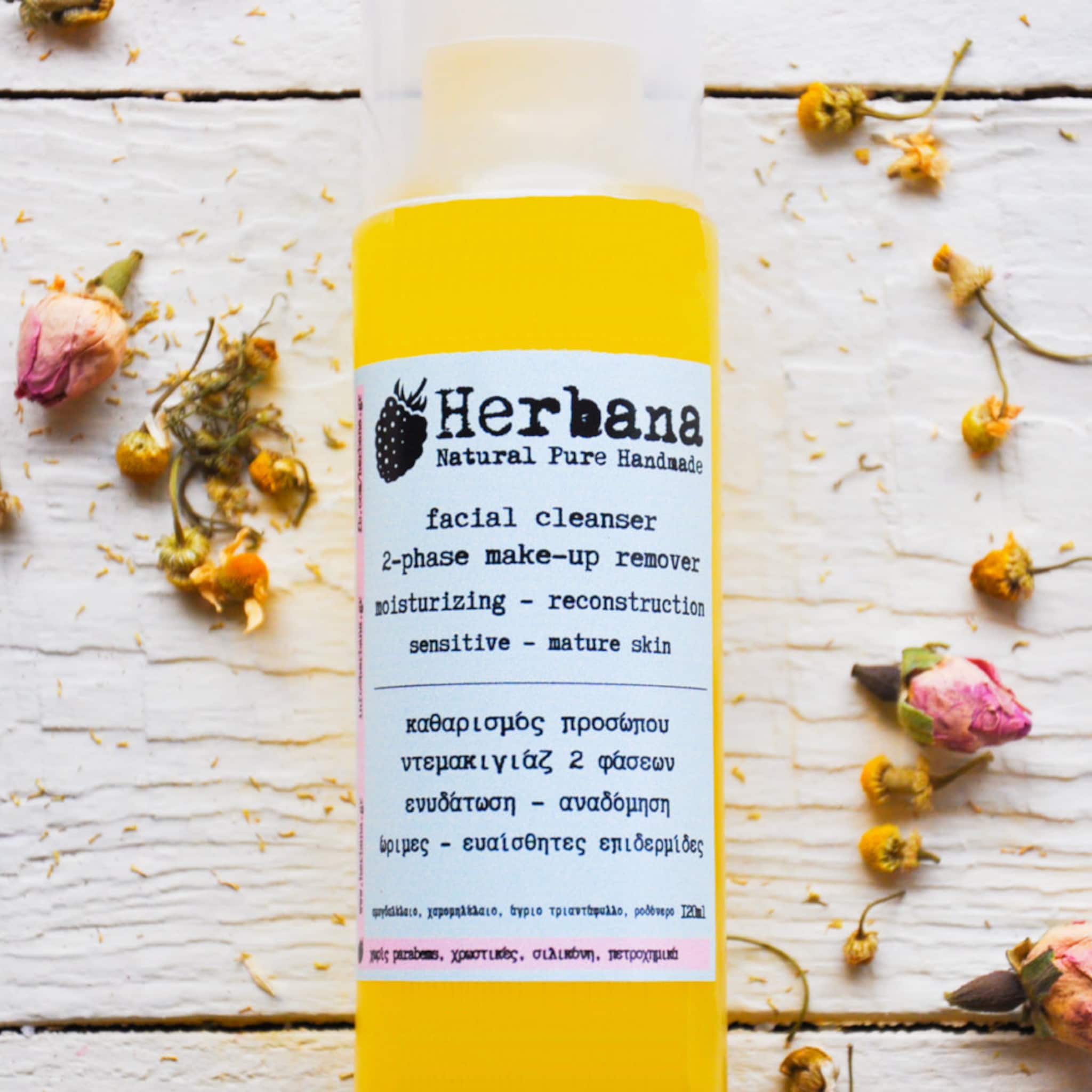 Facial cleanser bottle with yellow liquid, white label, and dried flowers on wood surface
