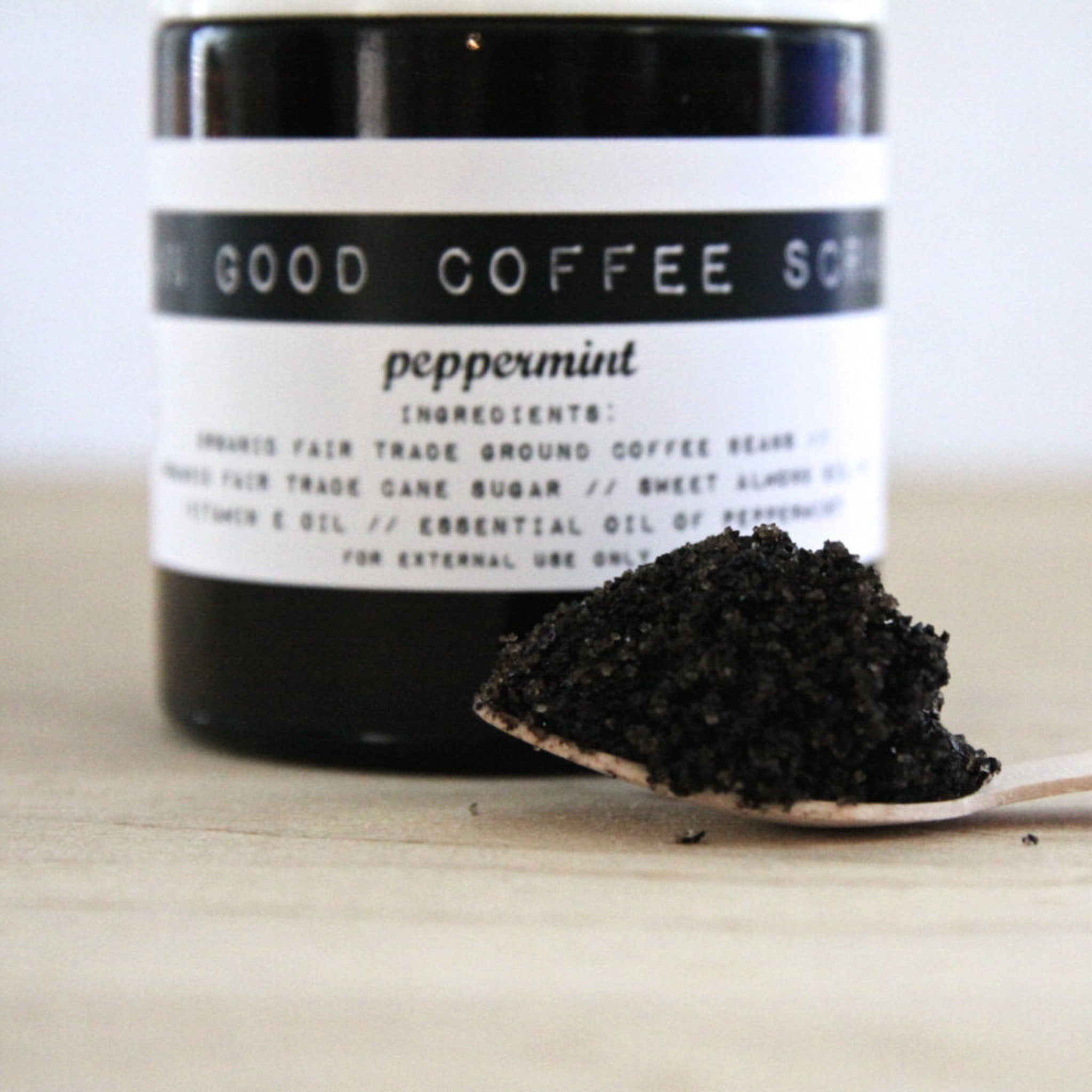 Coffee scrub in black jar with white label, peppermint ingredients, and wooden spoon