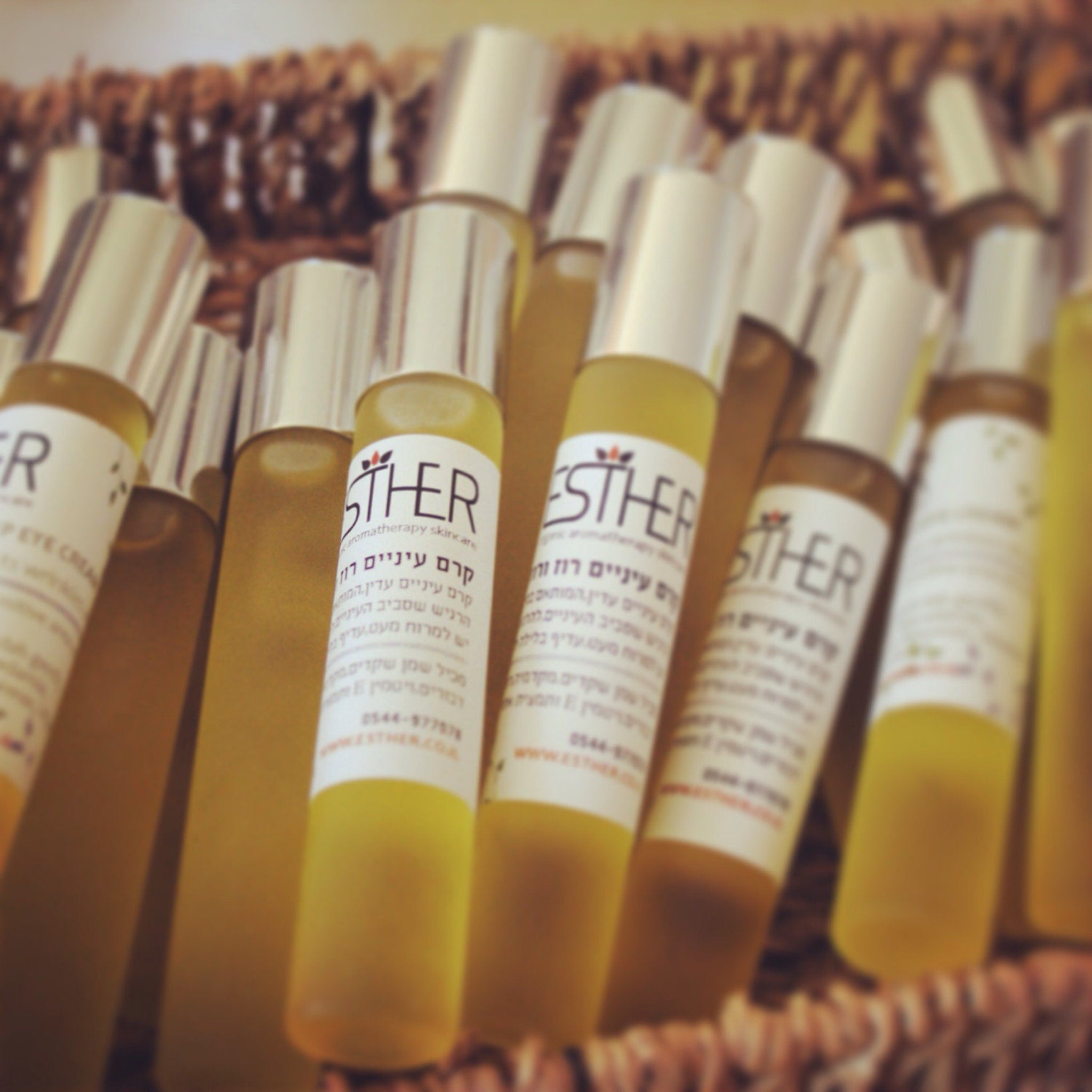 Bottles of yellow liquid with silver caps and white labels, "ESTHER" brand visible, in a woven basket.