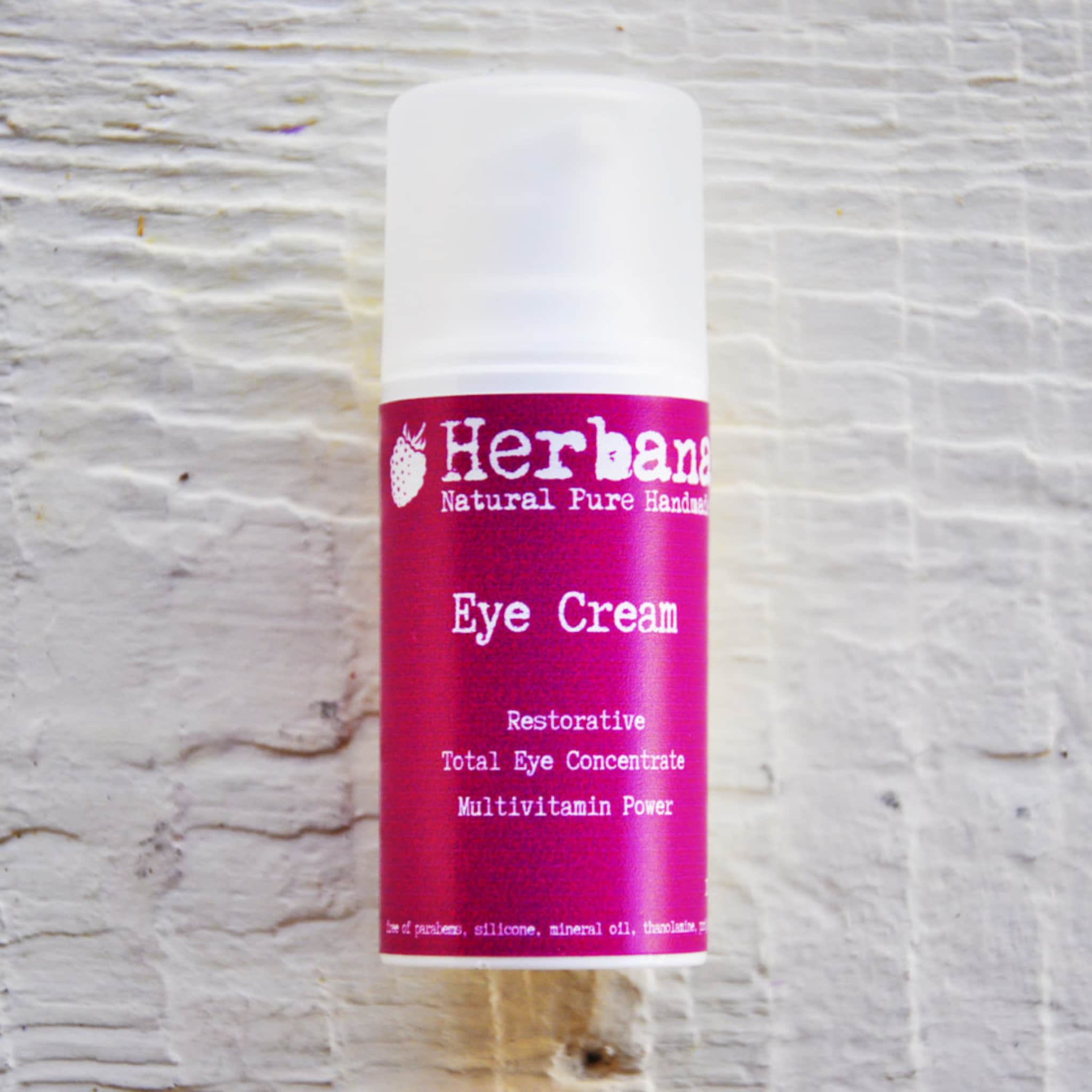 Eye cream bottle with white cap, magenta label, and Herbana brand text