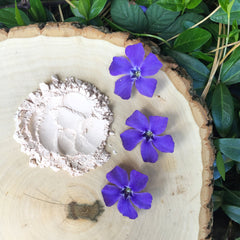 Powdered substance with light beige color on a wooden surface with purple flowers and green leaves