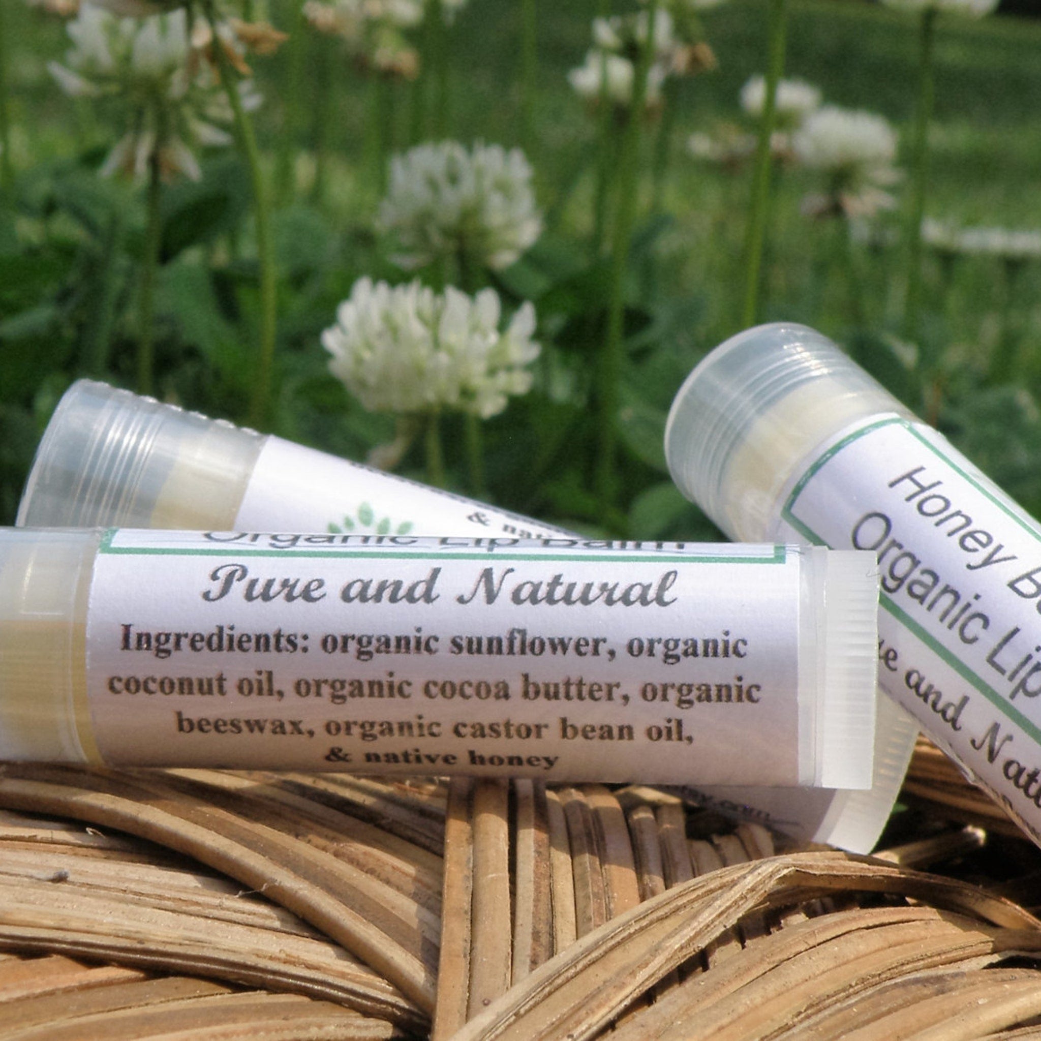 Lip balm tubes with white labels, clear plastic, and natural background of flowers and woven basket