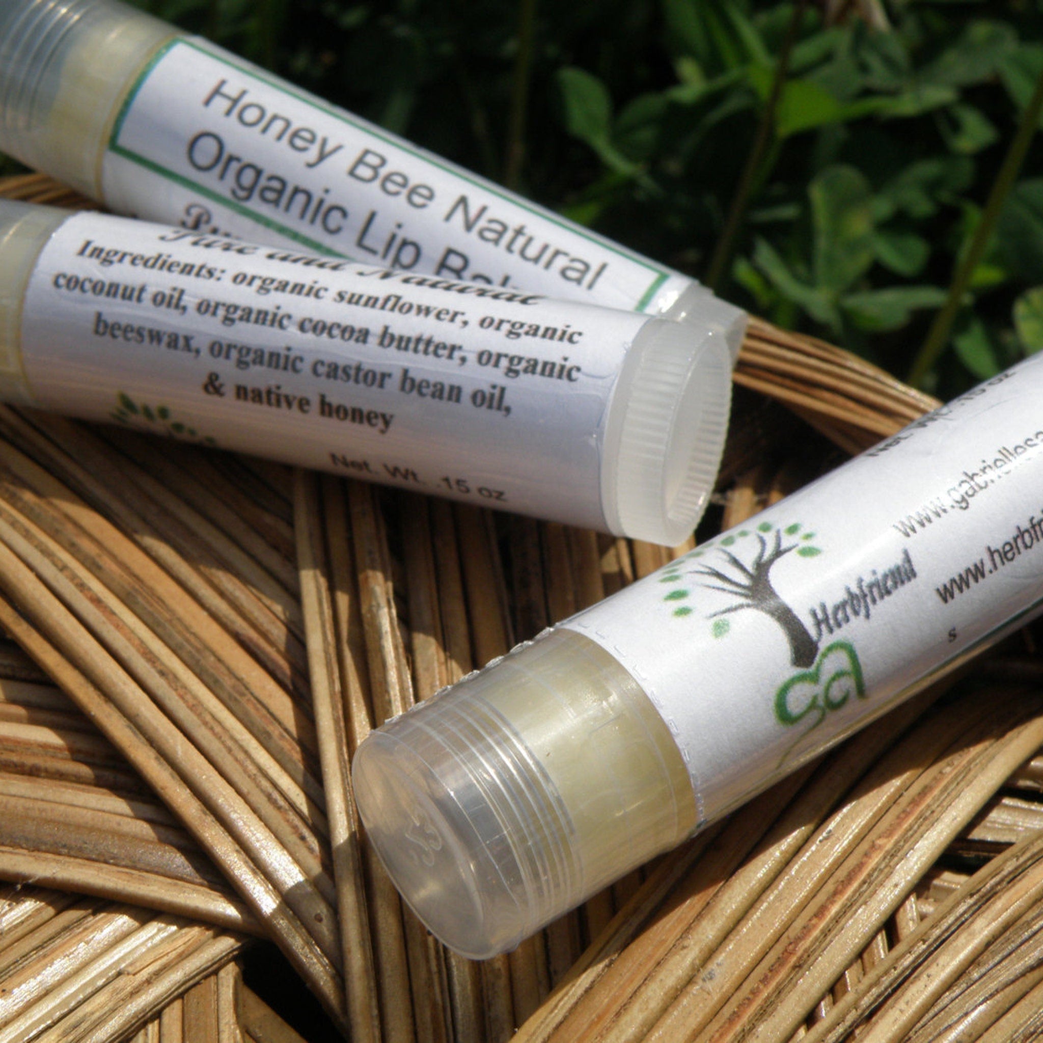 Lip balm tubes with white labels, clear caps, and Herbfriend logo on a woven surface