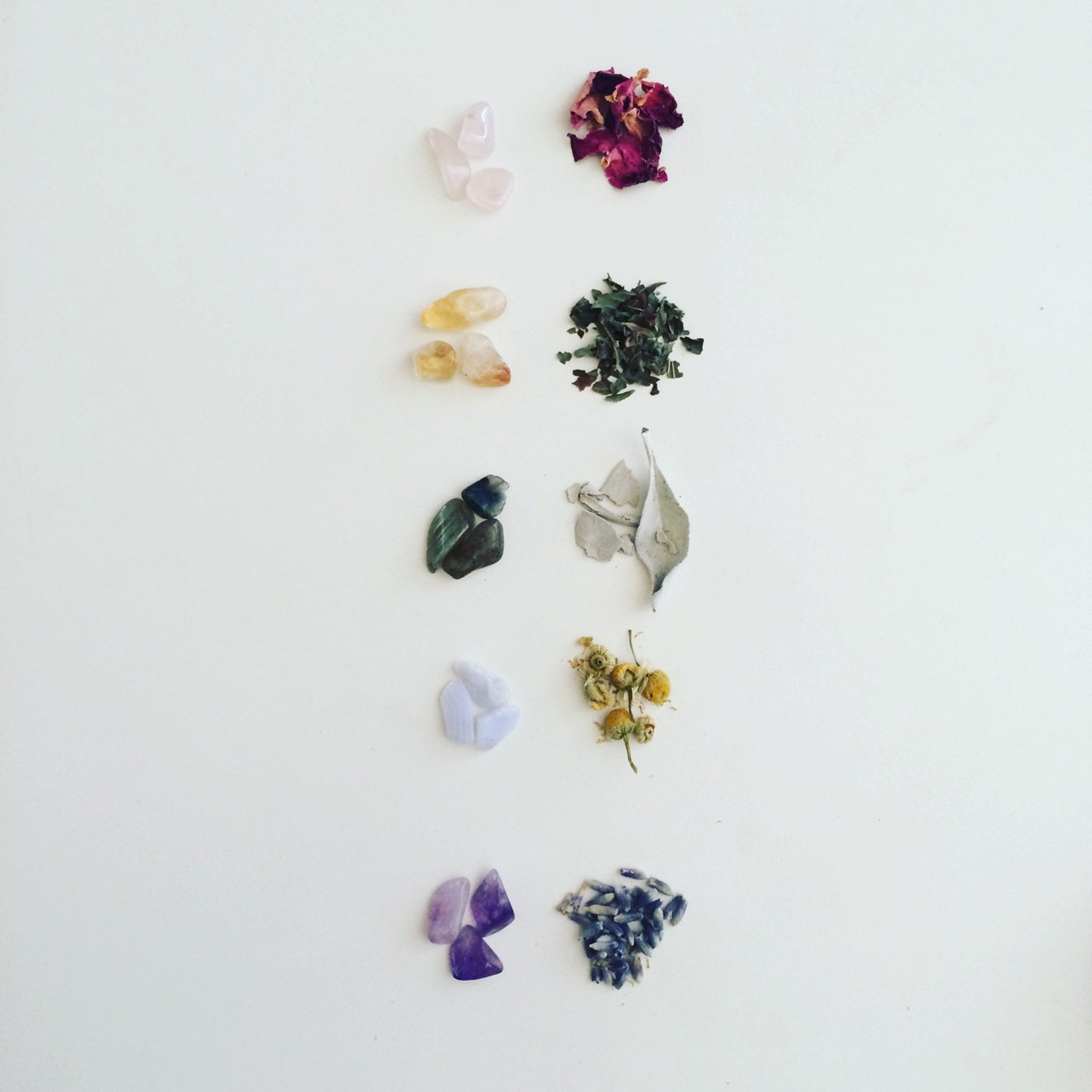 Crystals and botanicals: pink, yellow, blue, and purple stones with dried flowers and herbs on white background