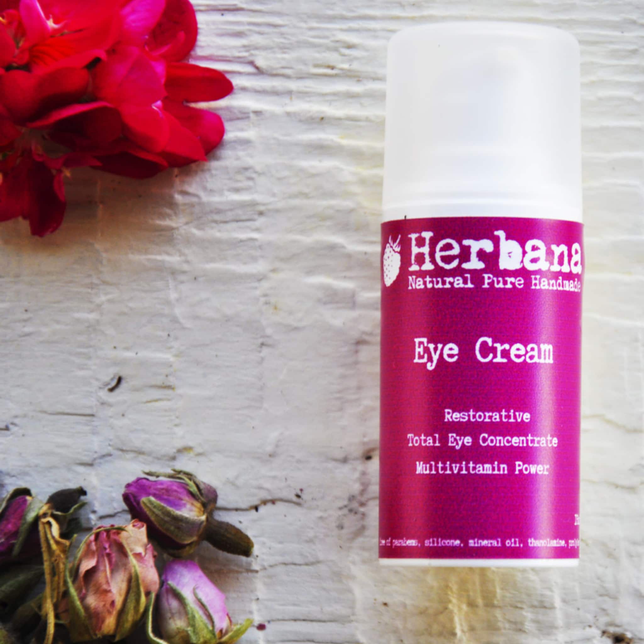 Eye cream bottle with white cap, pink label, and Herbania brand text on textured background