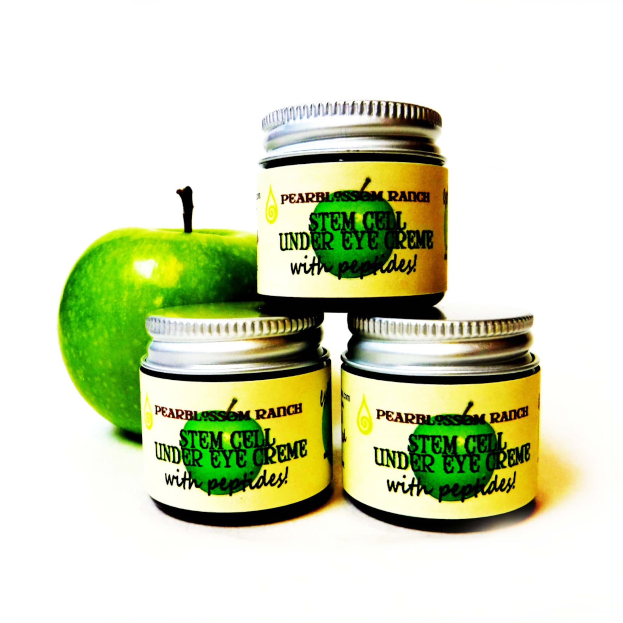 Eye cream jars with silver lids, yellow labels, and green apple, "PEARBLOSSOM RANCH" text visible