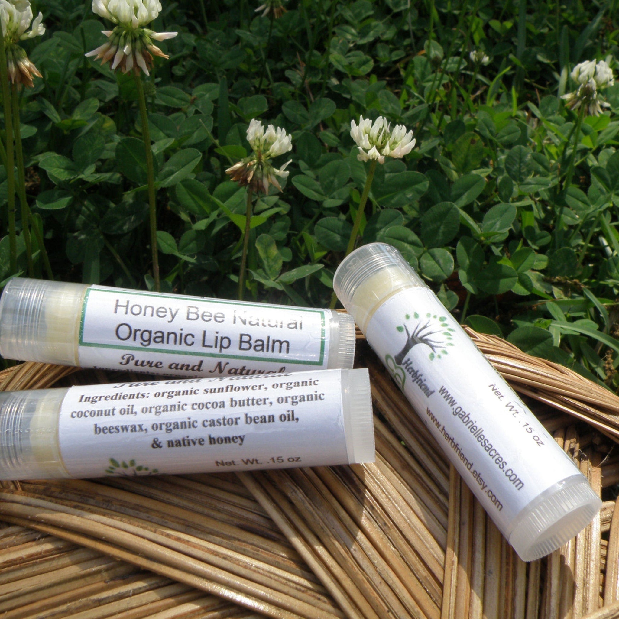Lip balm tubes with white labels, clear plastic, and "Herbfriend" branding, on woven surface